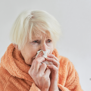 Dame âgée souffrante enroulée dans un plaid orange et en train de se moucher le nez.