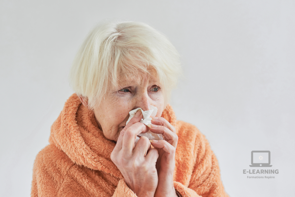 Dame âgée souffrante enroulée dans un plaid orange et en train de se moucher le nez.
