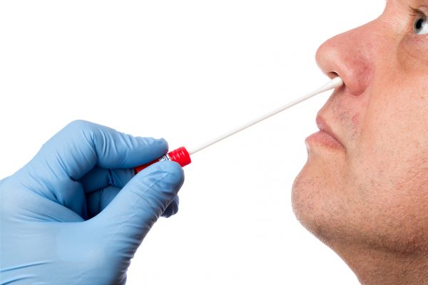 Zoom sur la main d'un soignant effectuant un prélèvement nasal sur un patient au moyen d'un écouvillon.