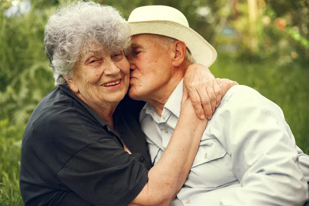 Un couple de personnes âgées amoureuses qui s'enlace devant un décor nature.